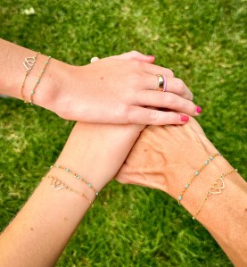 Four arms adorned with various minimalist bracelets, showcasing a mix of gold and colorful designs against a grassy background.