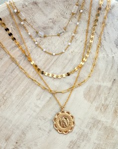 A collection of layered gold necklaces featuring various styles, including delicate chains and a central pendant, displayed against a neutral background.